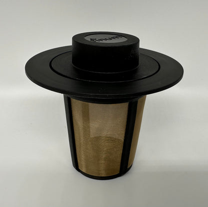 A top-down view of a black and gold coffee filter with a wide brim and circular lid, designed for brewing organic coffees
